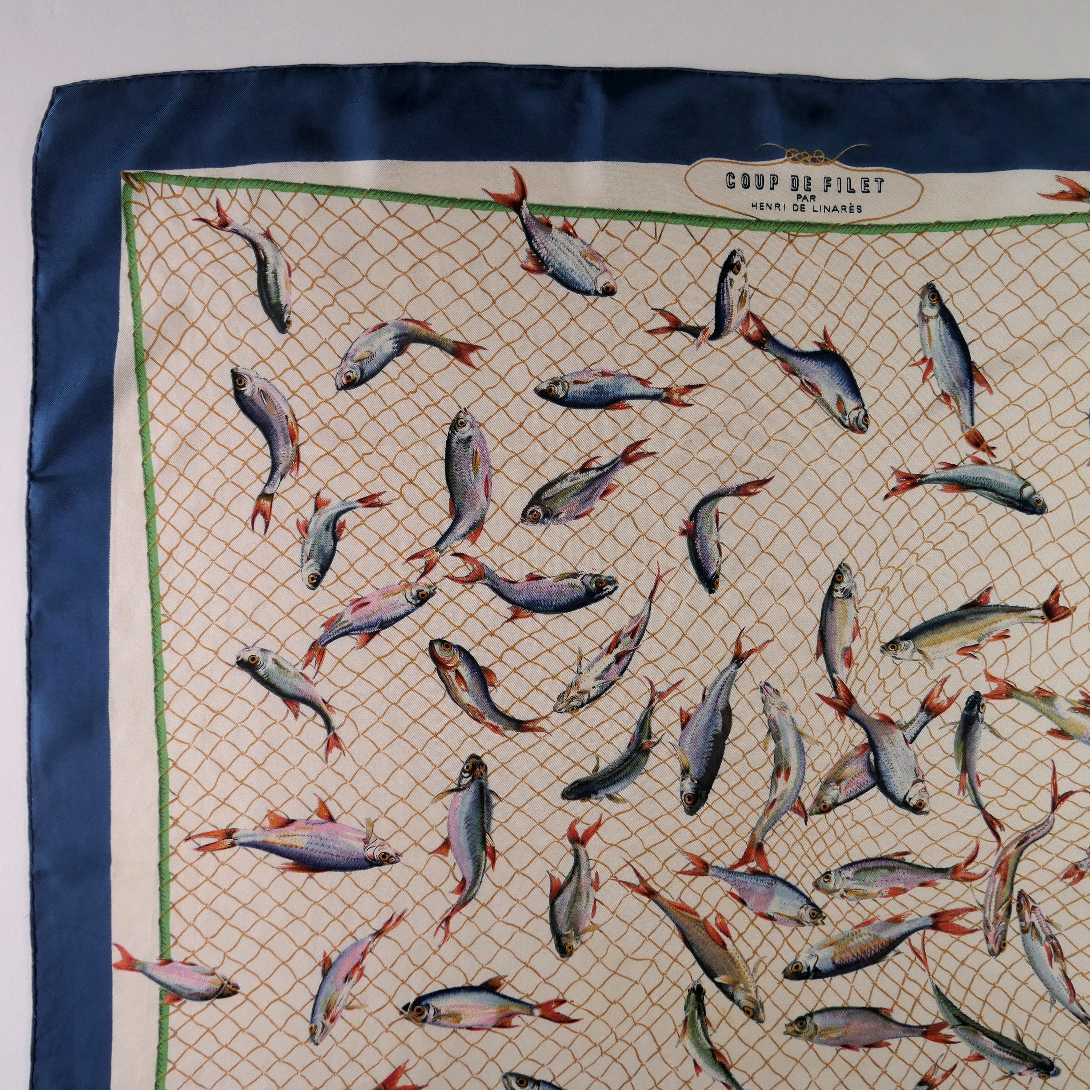 Carré Hermès Coup de Filet 90 cm soie, détail drapé et bordure bleu pétrole roulottée
