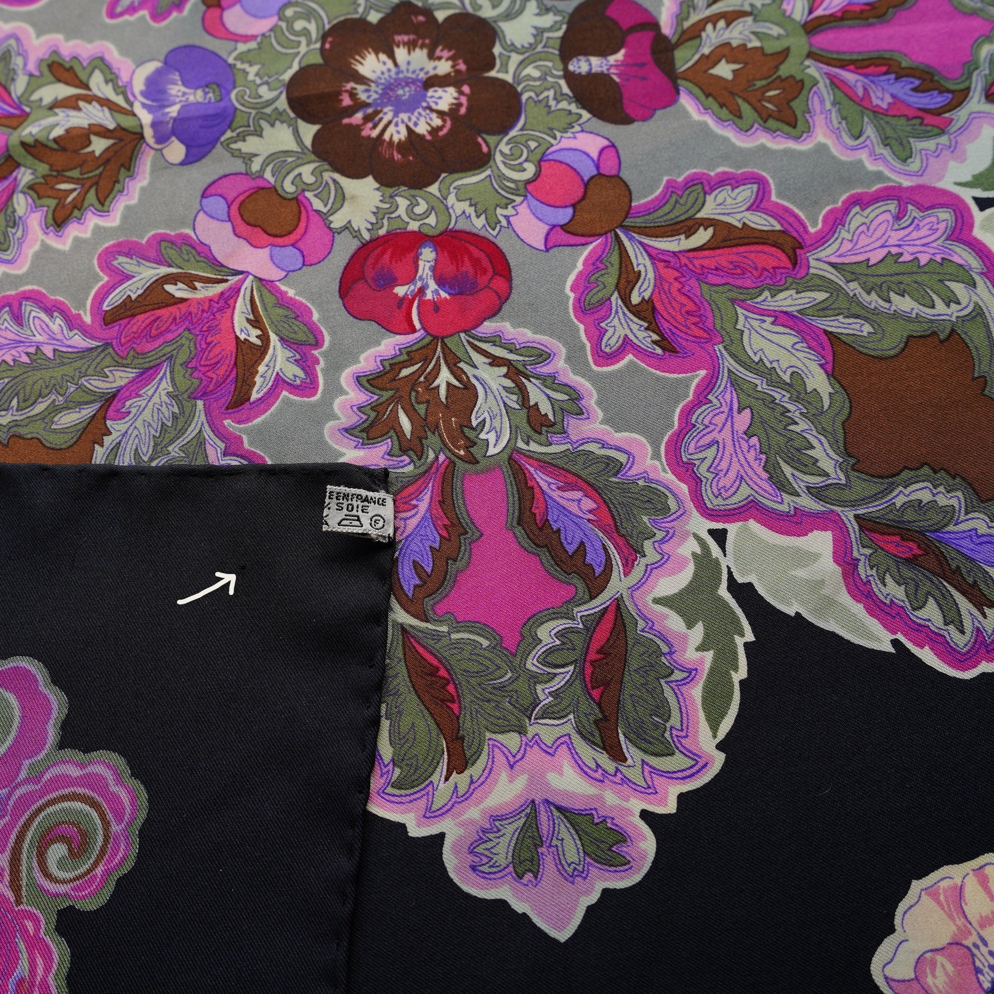 Gros plan sur un coin du foulard "Anémones", une flèche montre un second micro-trou sur le tissu.