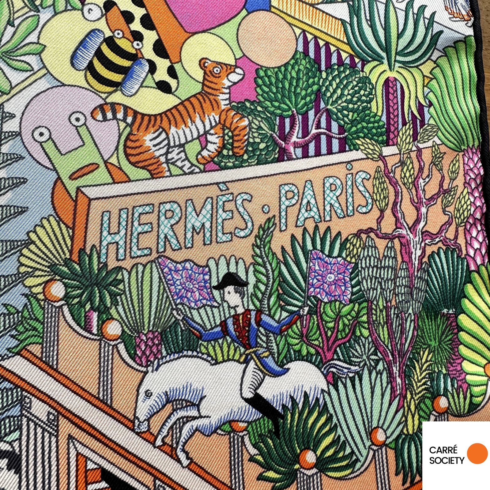 inscription « Hermès Paris » parmi la végétation et les animaux, sur fond architectural.