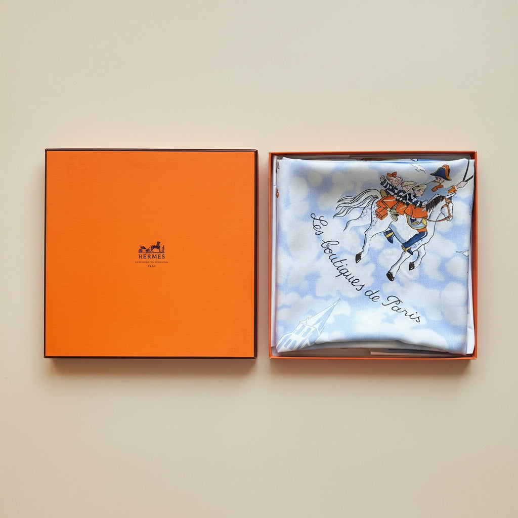 Boîte orange Hermès et foulard en soie Les Triplés plié à l'intérieur.