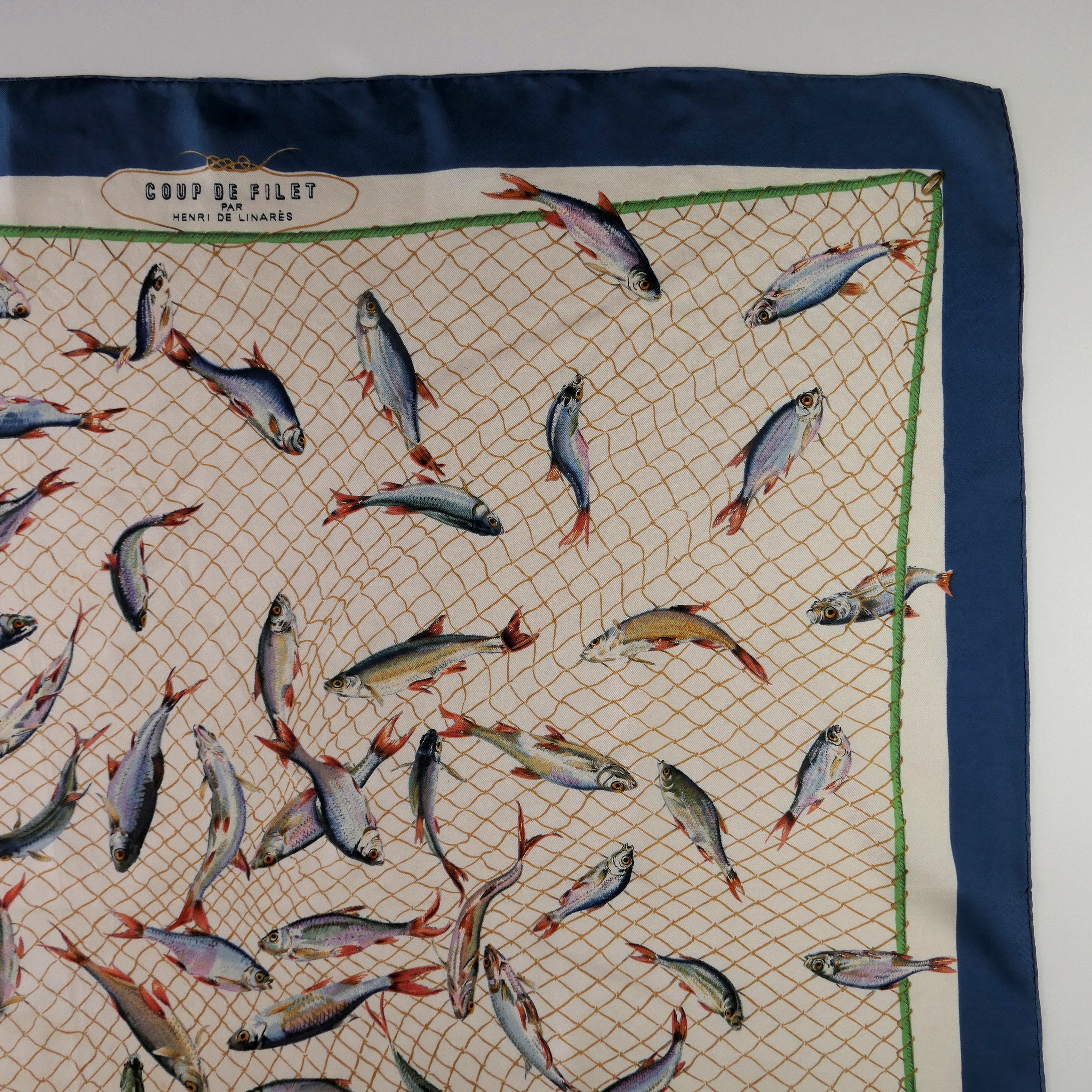 Carré Hermès Coup de Filet 90 cm soie, détail poissons argentés dans filet, fond écru bleu pétrole