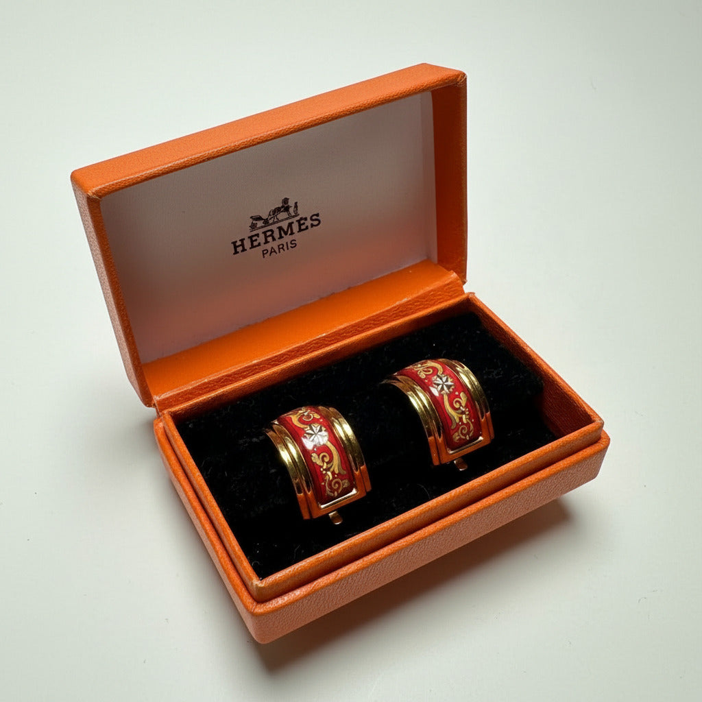 Paire de clips d'oreilles Hermès vintage en émail rouge et or, modèle large, présentés ouverts dans leur boîte orange   d'origine.