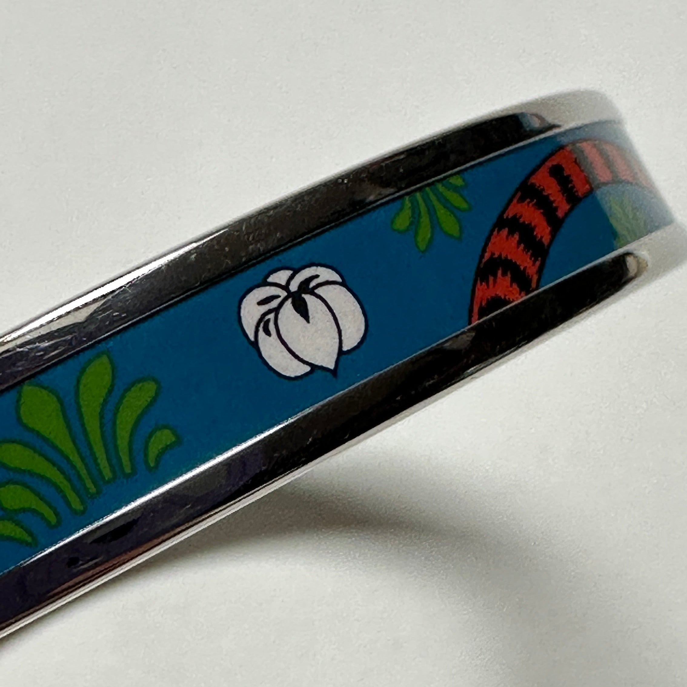 Gros plan sur l'émail imprimé Hermès : motif Tigre Royal avec queue de tigre et fleurs sur fond bleu lagon.