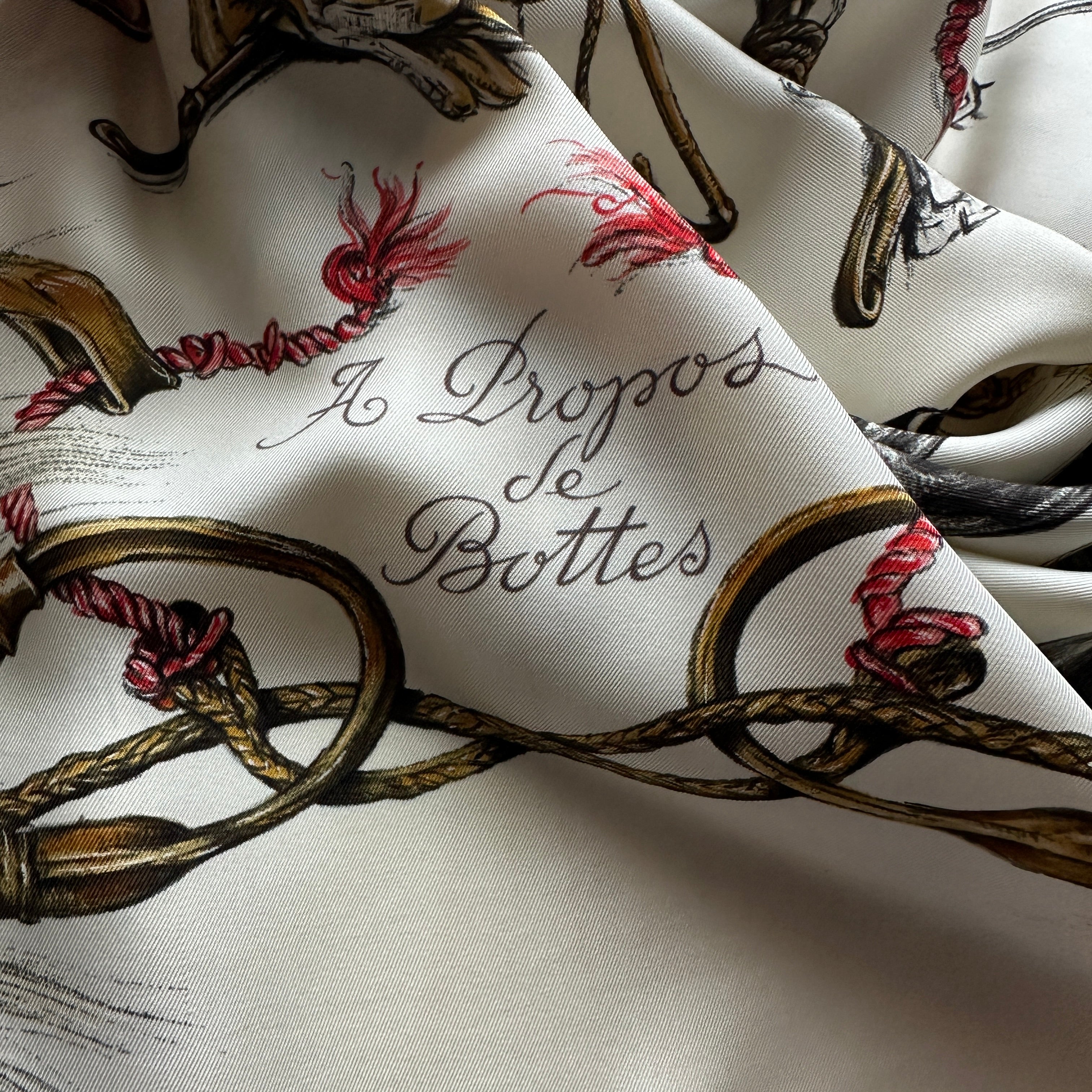 Le foulard drapé artistiquement, mettant en valeur le lettrage élégant et le contraste entre le fond crème et les touches de rouge.