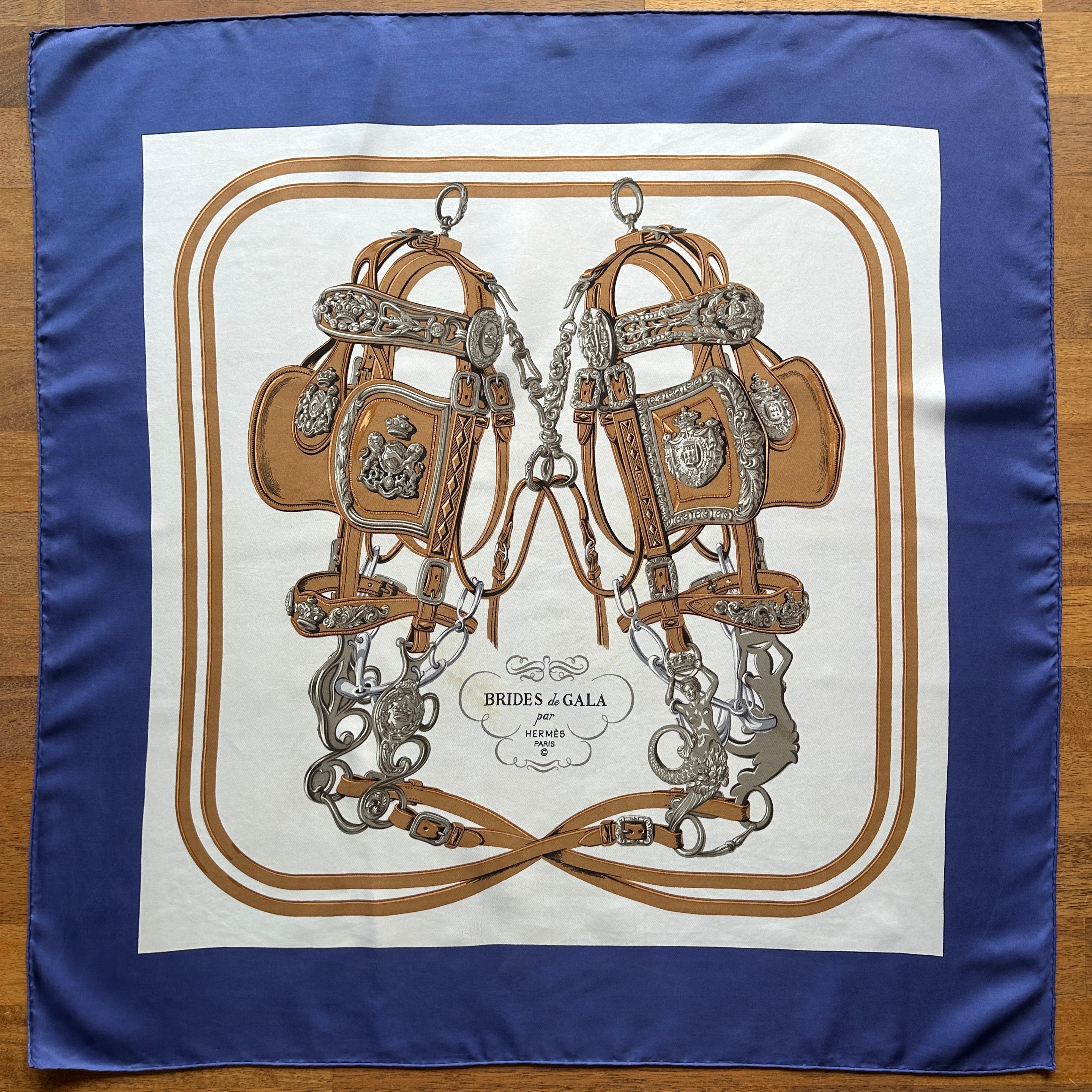 vue d'ensemble du foulard Hermès brides de gala déplié à plat fond crème entourage bleu lavande