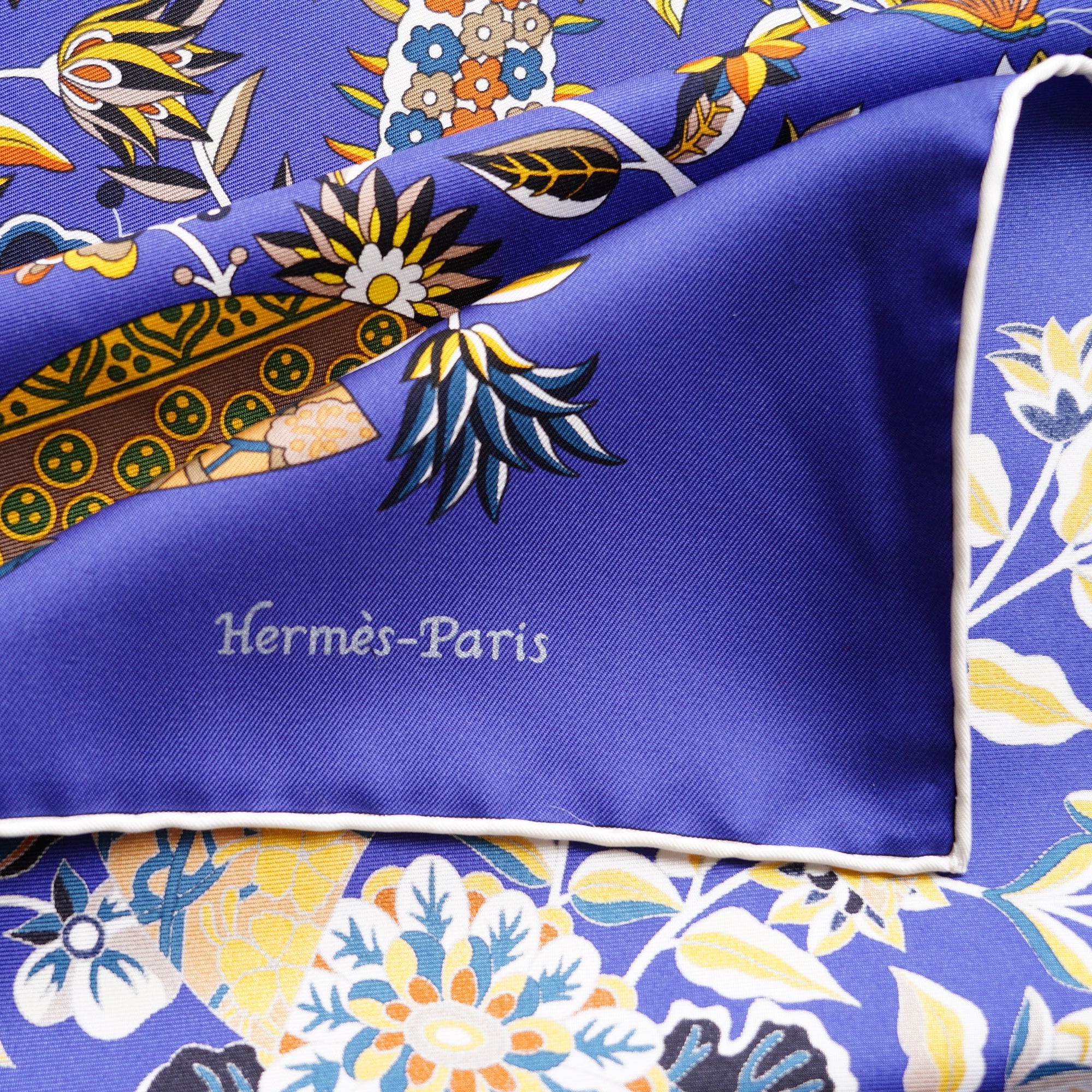 Gros plan sur la signature "Hermès-Paris" sérigraphiée dans le coin du foulard en soie bleu roi avec bordure blanche.