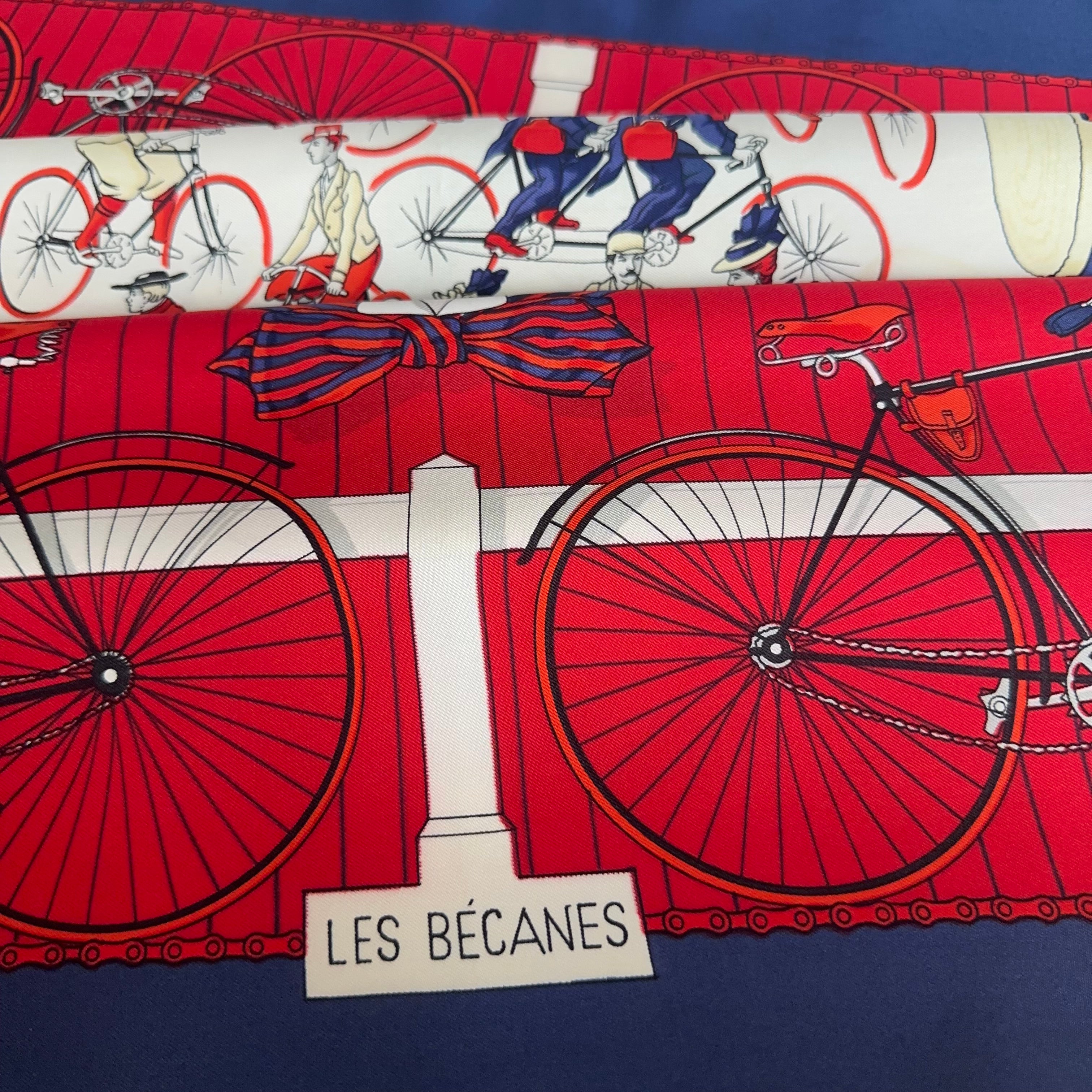 Détail du foulard plié montrant le titre "LES BÉCANES" dans un cartouche blanc en bas du dessin.