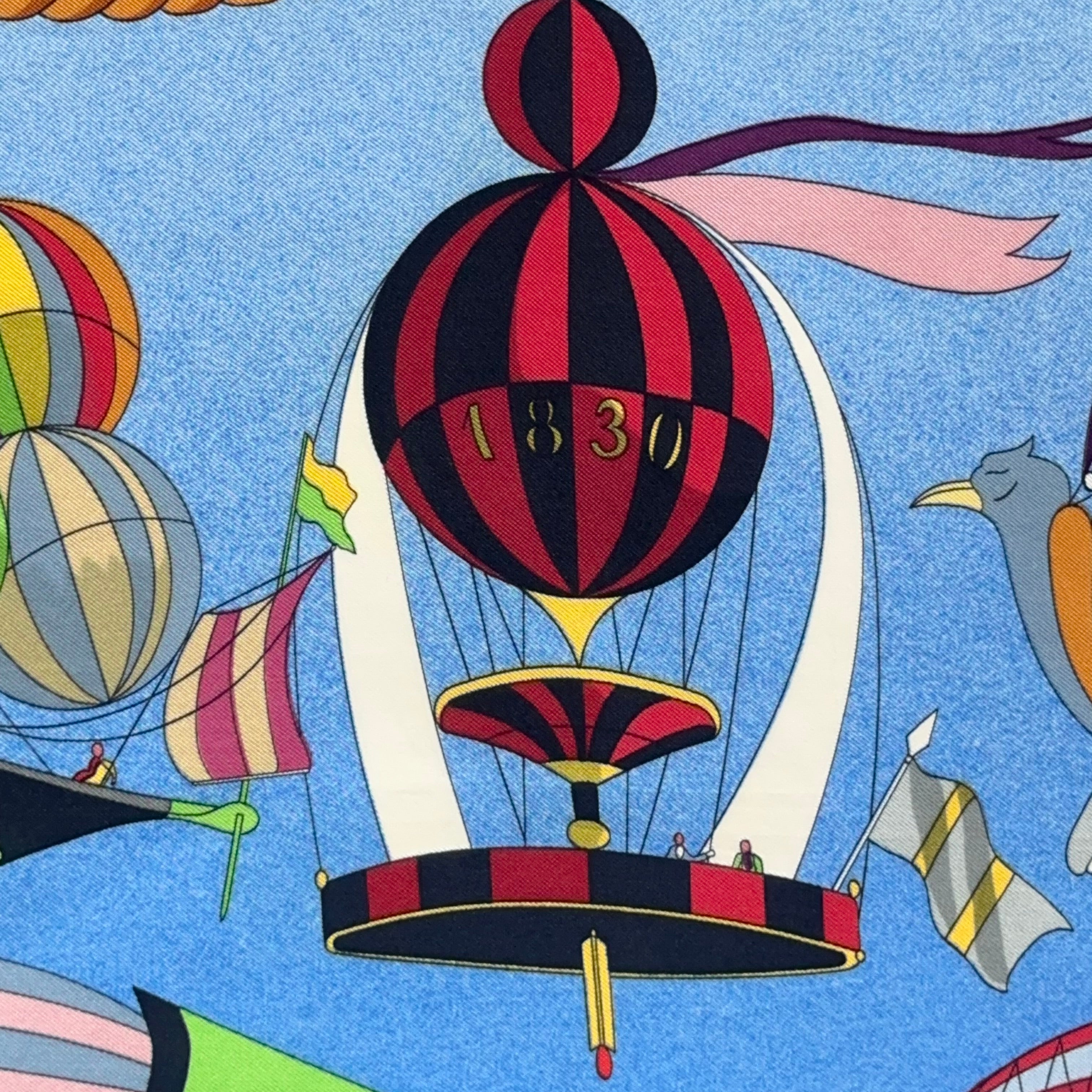 Gros plan sur une machine volante rouge et jaune à hélice datée "1850", détail de la corde torsadée or qui borde le foulard.